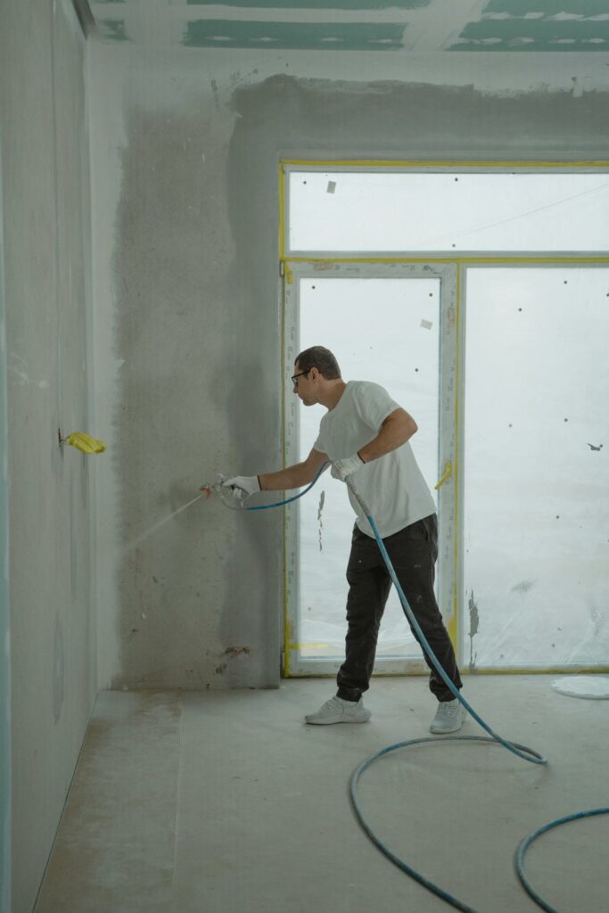 Technician performing spray application in an office corner during office remodeling, coating walls as part of interior renovation work.